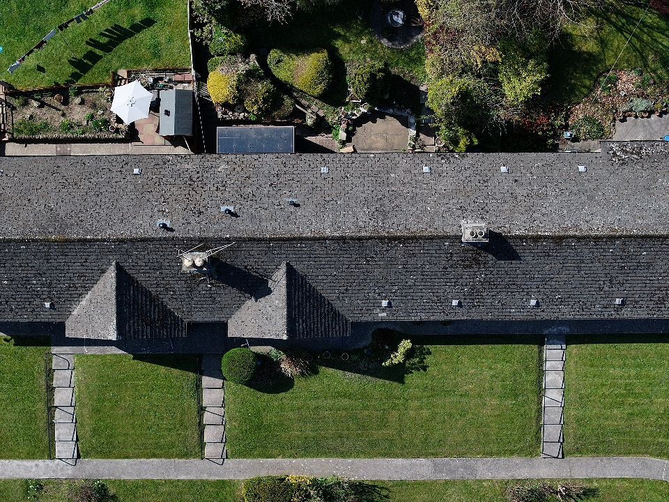 Bird's eye view of a long stone building with grey roof and pillars along a walkway.