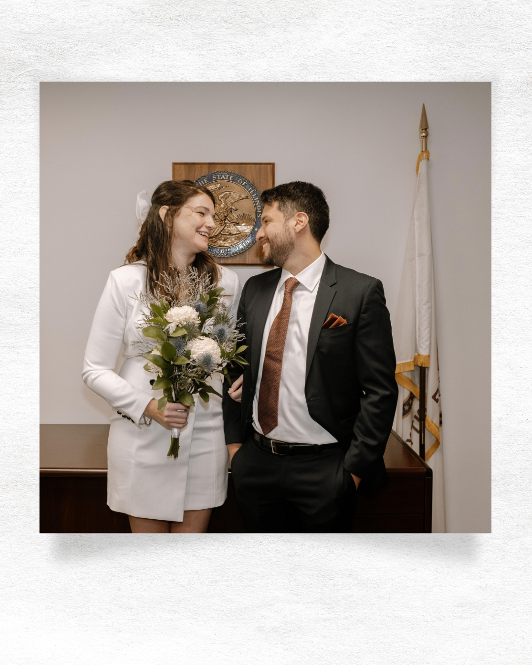 A couple in wedding attire shares an intimate moment against a light background with modern minimalist decor.