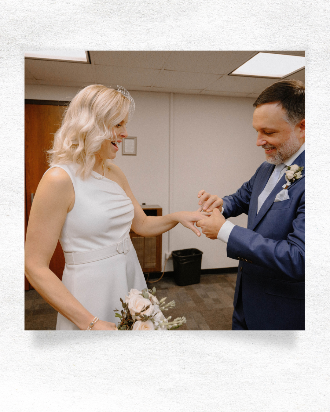 A couple in a white dress and navy suit exchanging rings during an intimate indoor church ceremony.