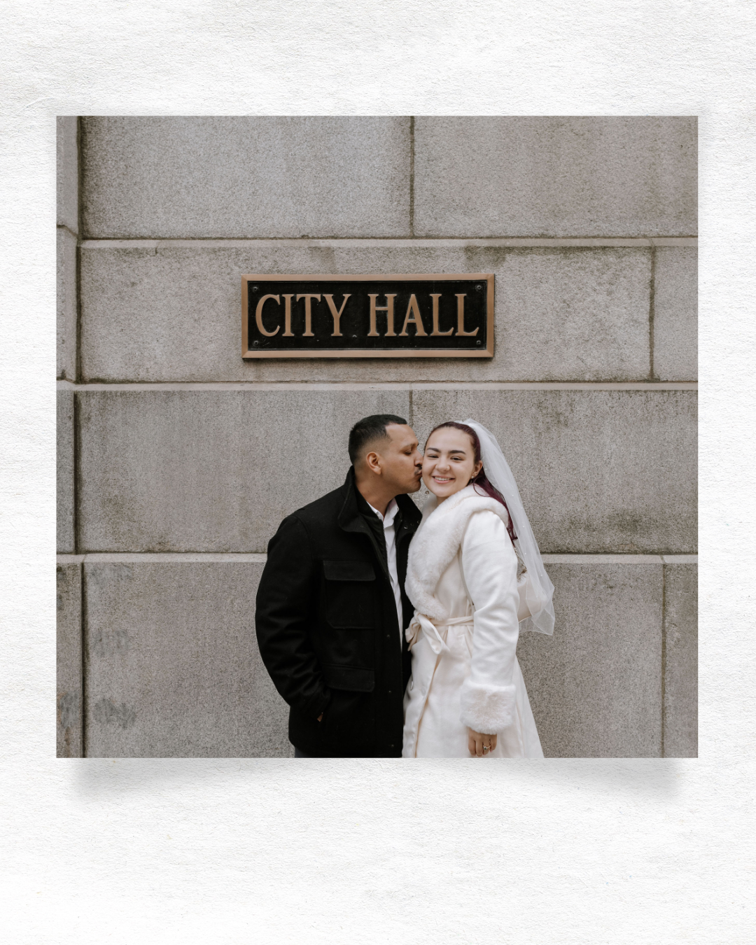 A couple poses lovingly against a city hall building wall during their wedding day.