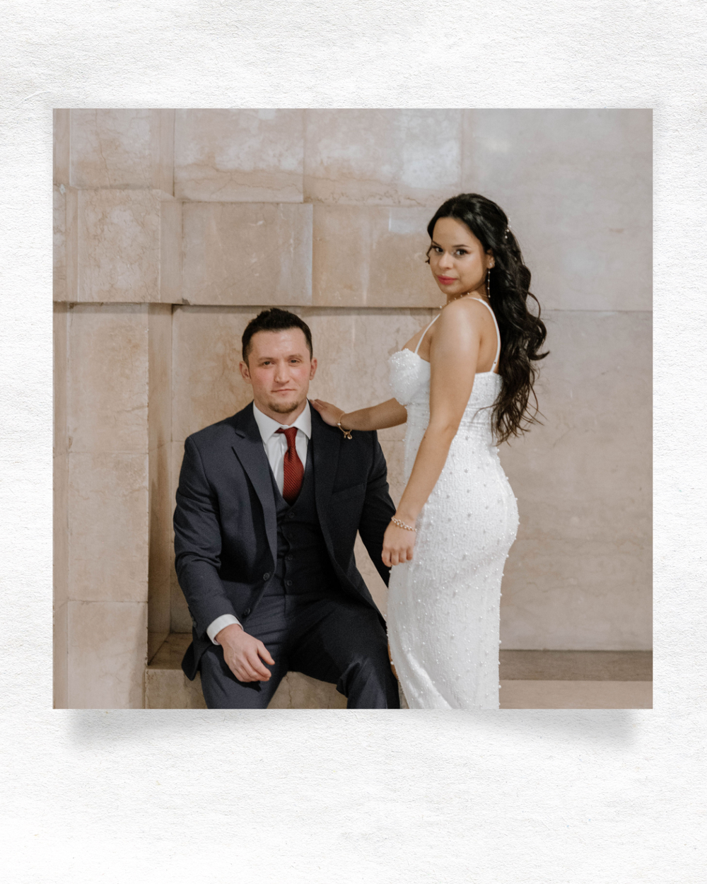 Newlywed couple poses for elegant wedding portrait with bride in white lace gown and groom in dark suit with red tie.