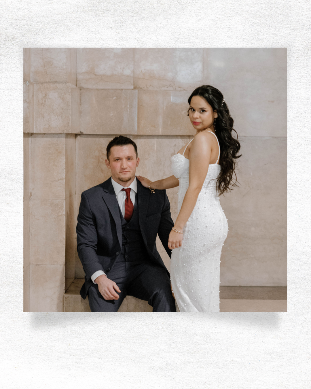 Newlywed couple poses for elegant wedding portrait with bride in white lace gown and groom in dark suit with red tie.