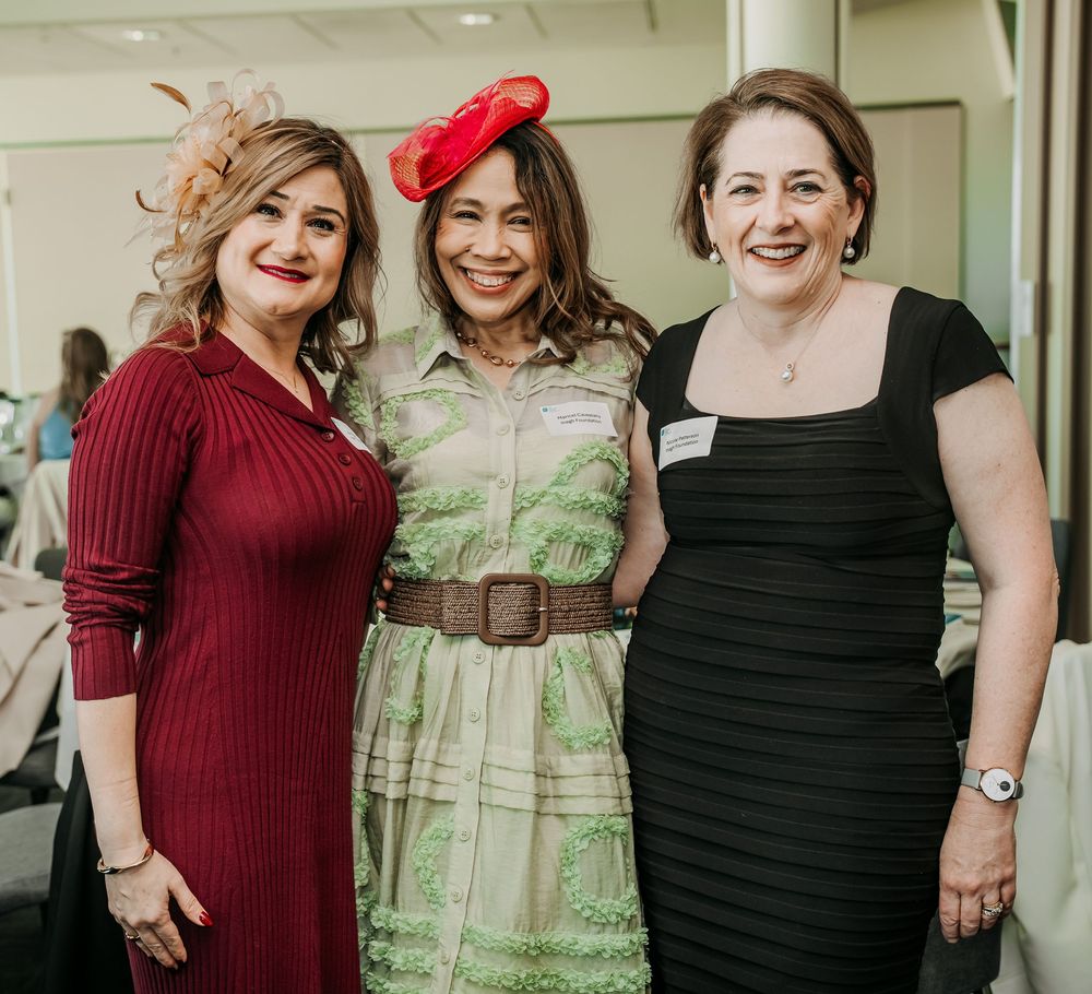 Three people at an event wearing a red sweater dress, green patterned dress, and black dress respectively.