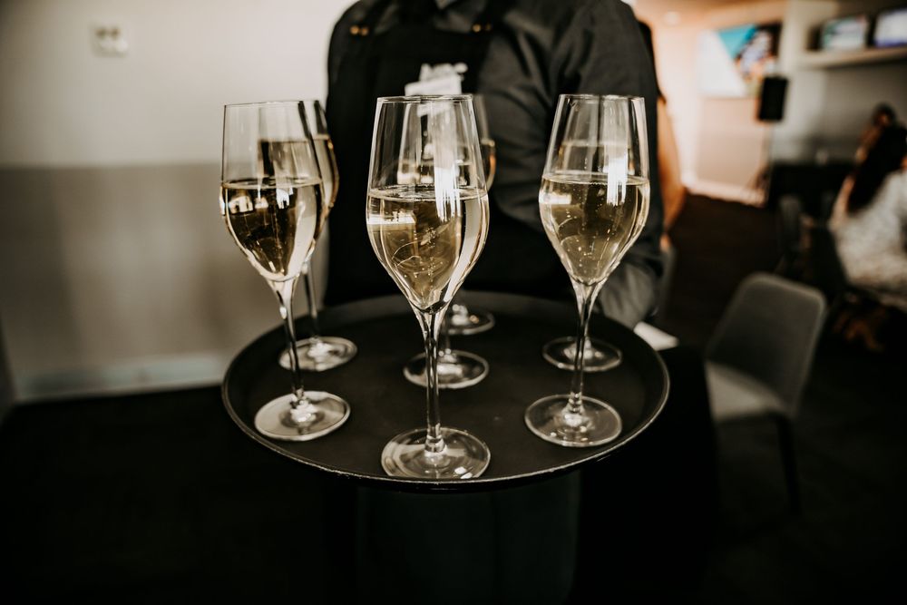 Server holds a black tray with three elegant champagne glasses filled with sparkling wine in a restaurant setting.