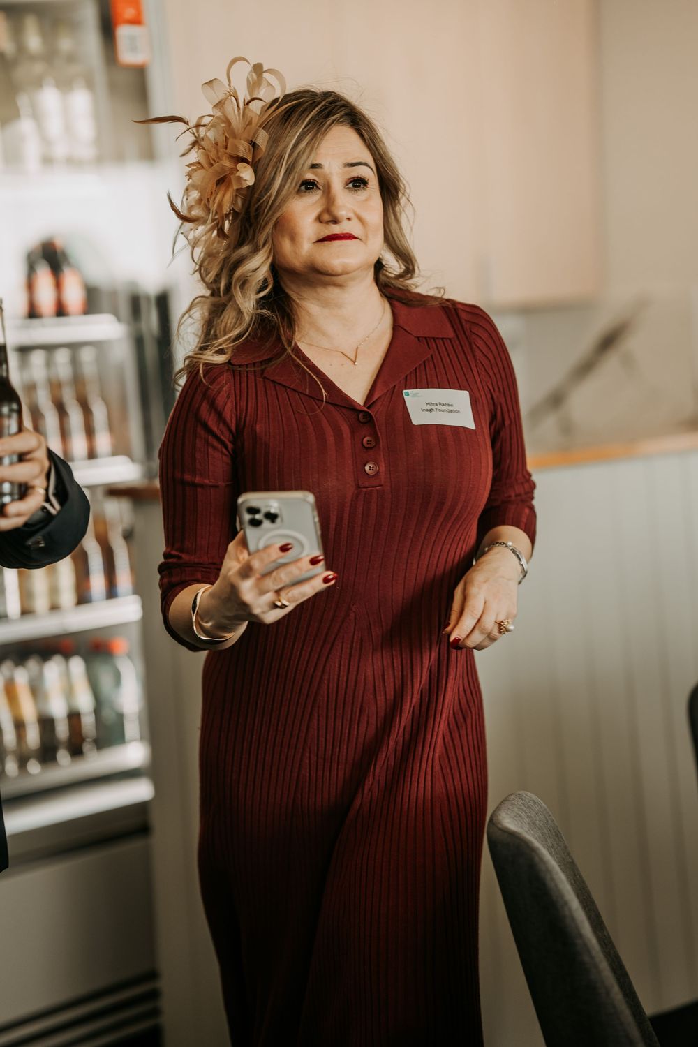 Woman in burgundy ribbed dress holding phone with decorative hair piece on while standing in retail space.