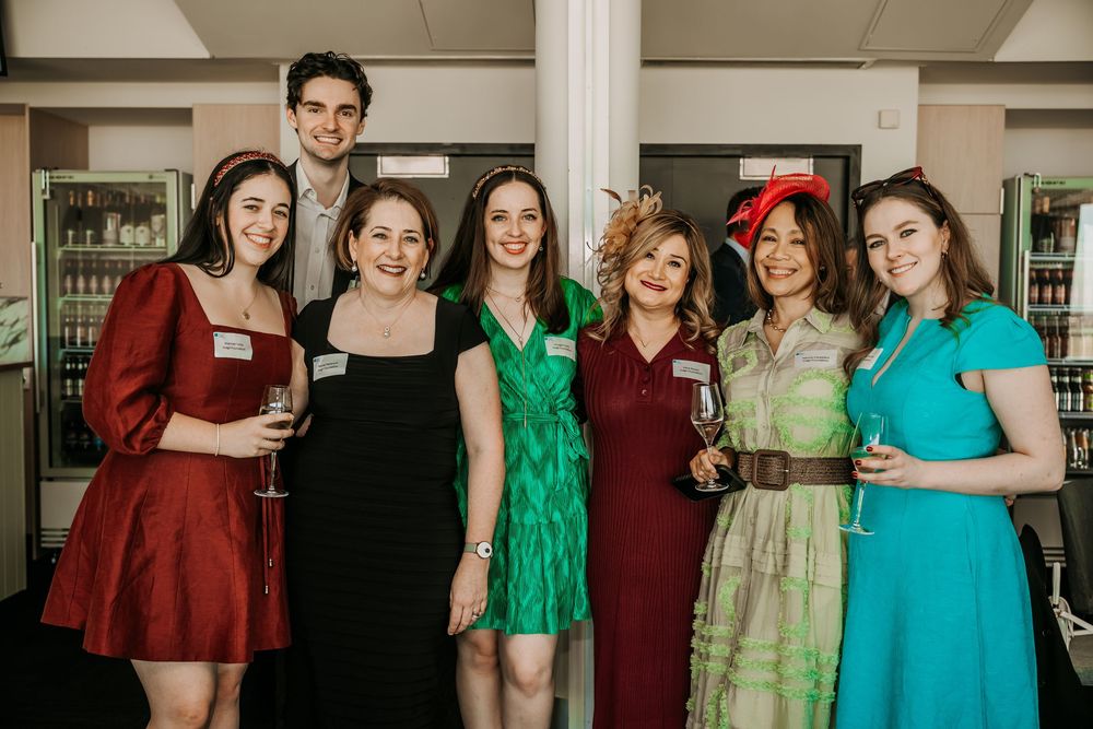 A group of people in formal attire poses together at a social event, wearing bright colors like green, turquoise and red.