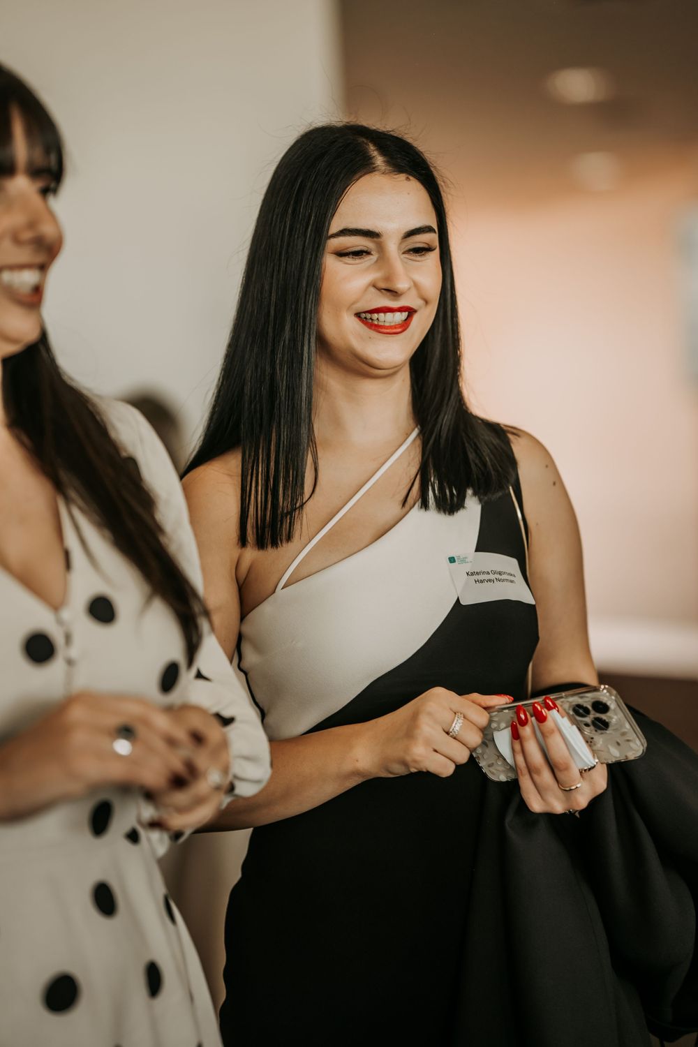 Joyful woman in a black and white asymmetrical outfit smiling while looking down at her phone.
