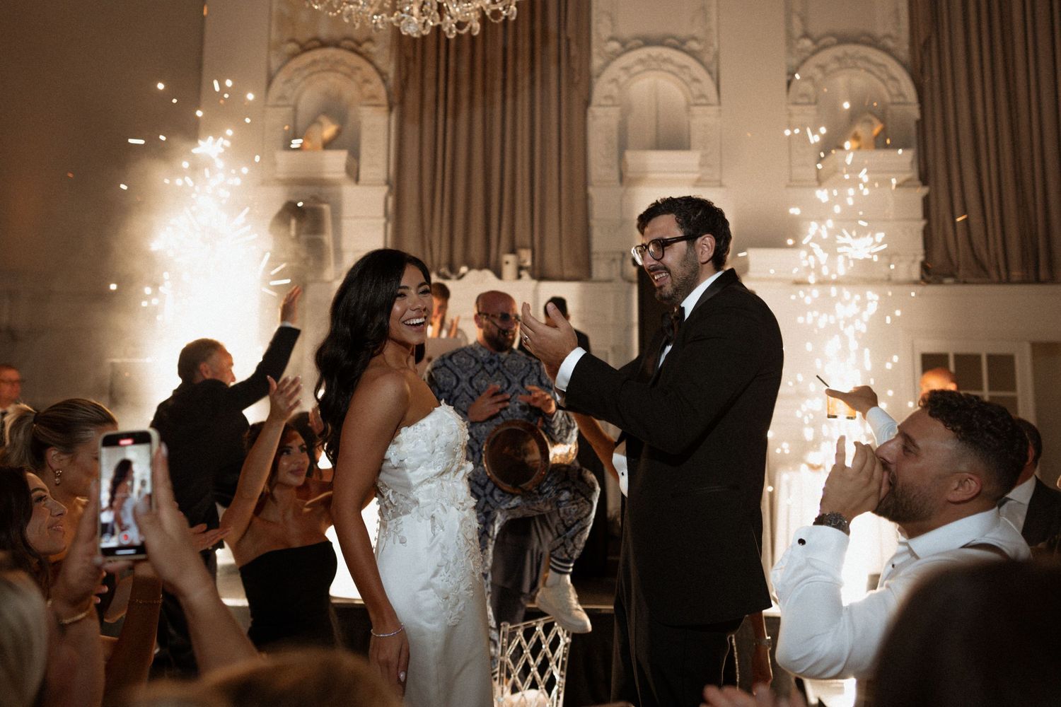 Close-up view of a couple embracing on their wedding day, showing details of a white dress and black tuxedo in sunlit setting.