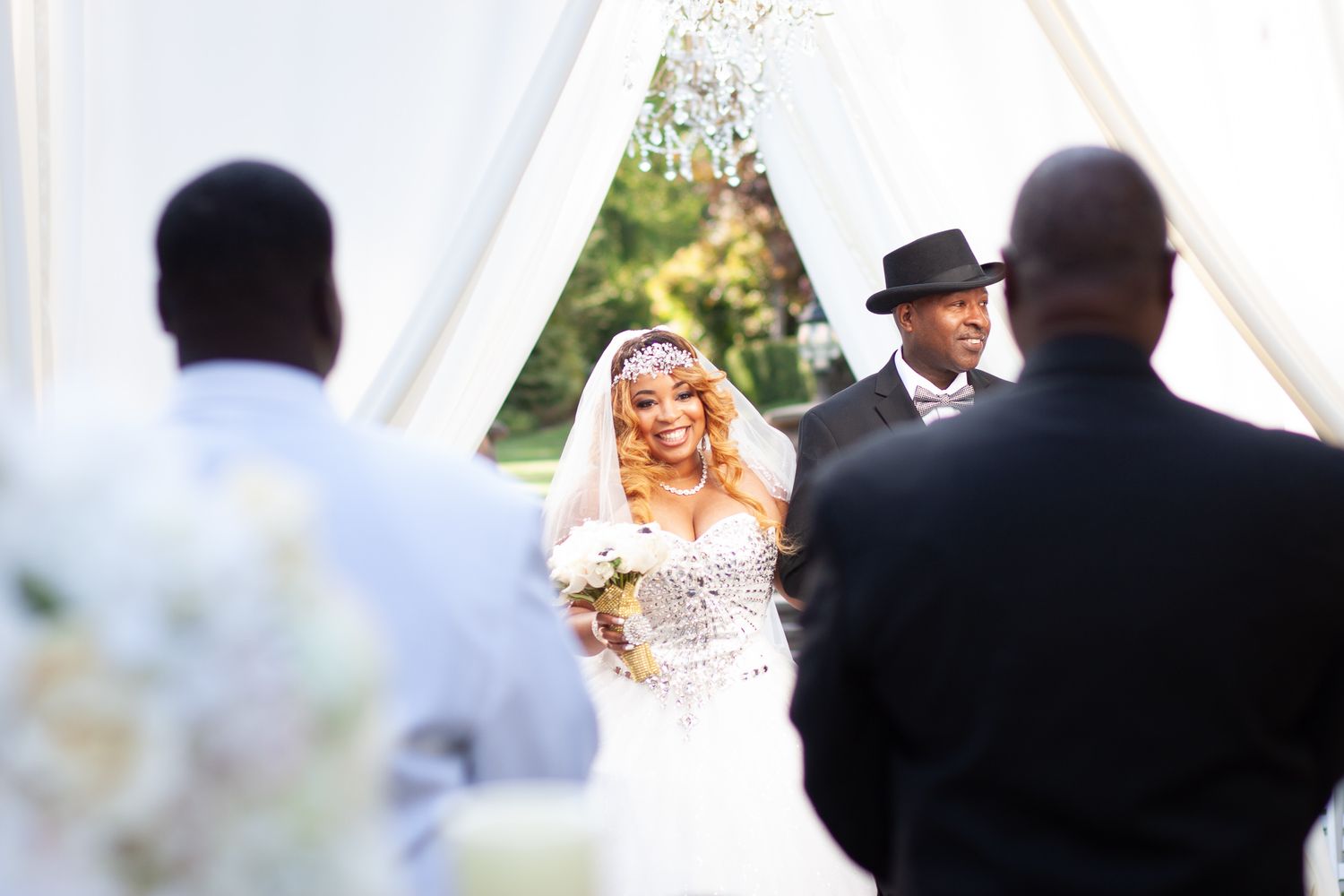 Happy couple exchanges vows during outdoor wedding ceremony under white fabric draping with natural sunlight.