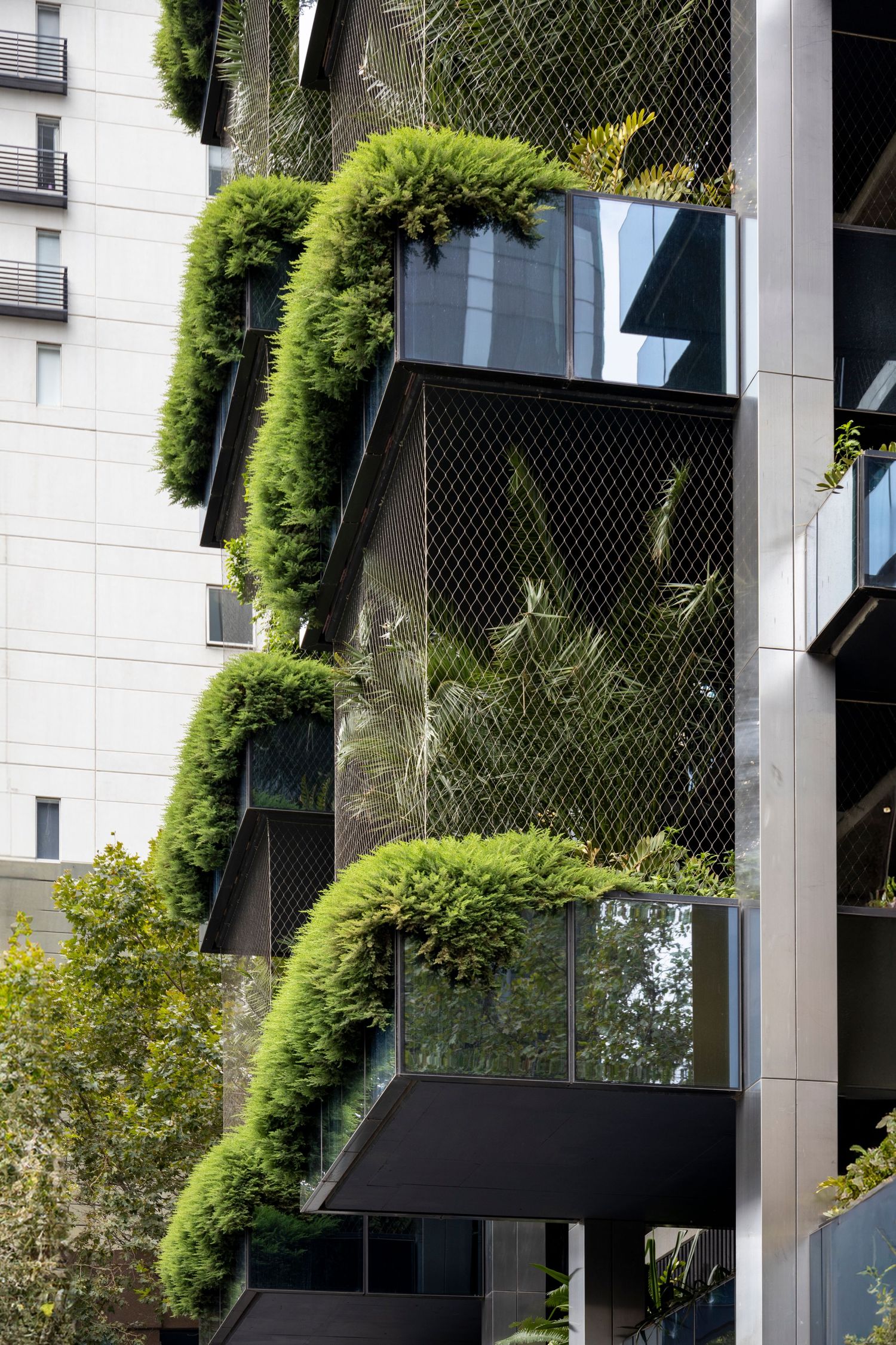 Apartment balconies bursting with lush cascading greenery over metal mesh façades.