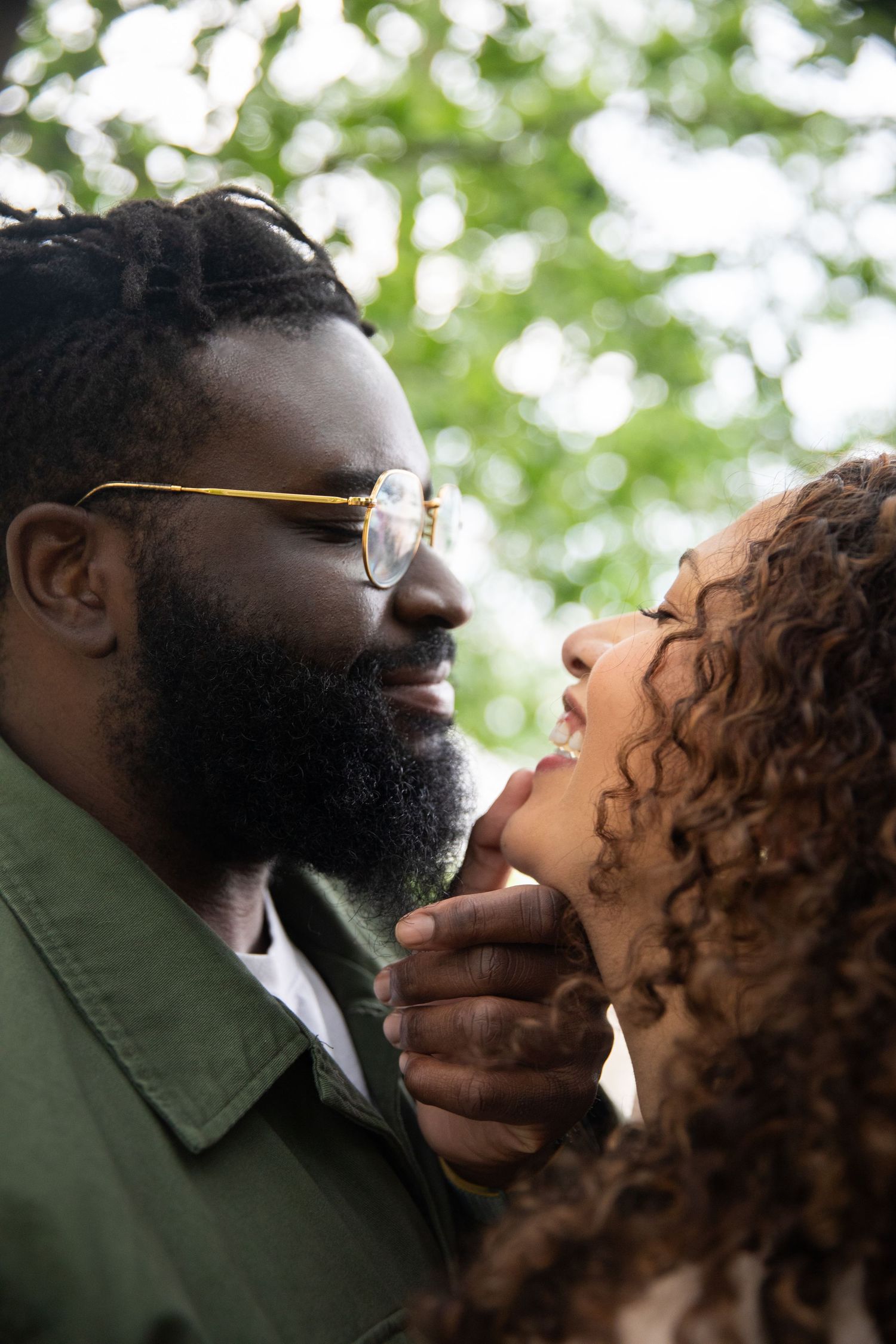 Intimate couple share tender moment outdoors with green bokeh background and soft natural lighting.