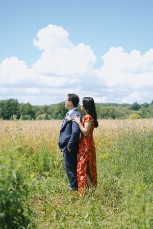 Couple stands back-to-back in sunny meadow during engagement photoshoot.