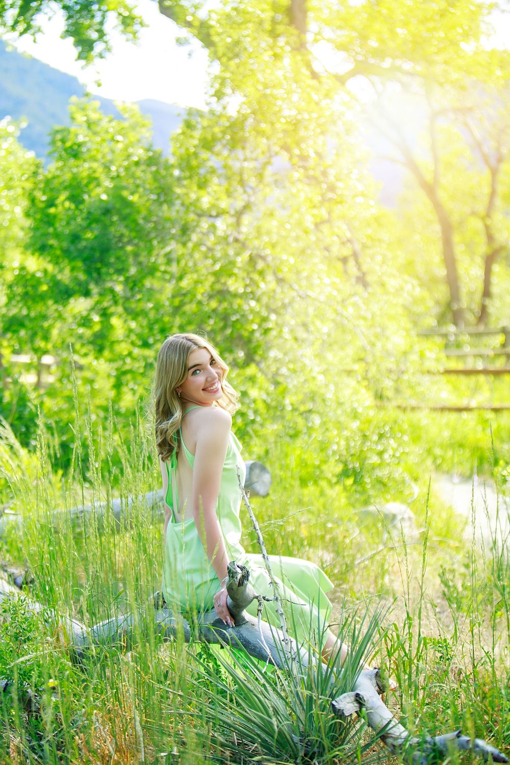 A person in a light green dress sitting in a sunny garden with lush greenery and flowers on a bright summer day.