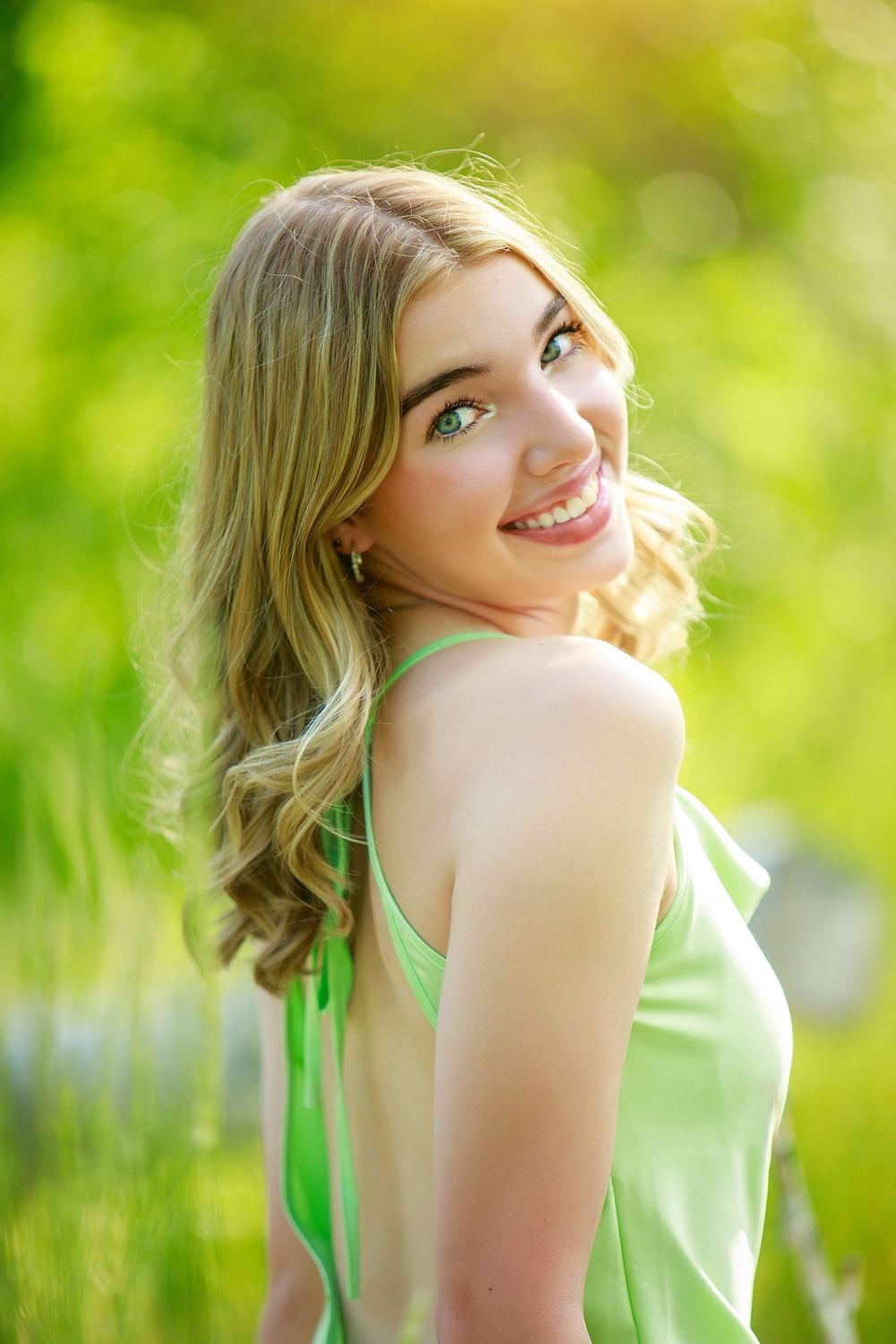 Portrait of someone in a green top smiling outdoors with soft bokeh and natural lighting in the background.