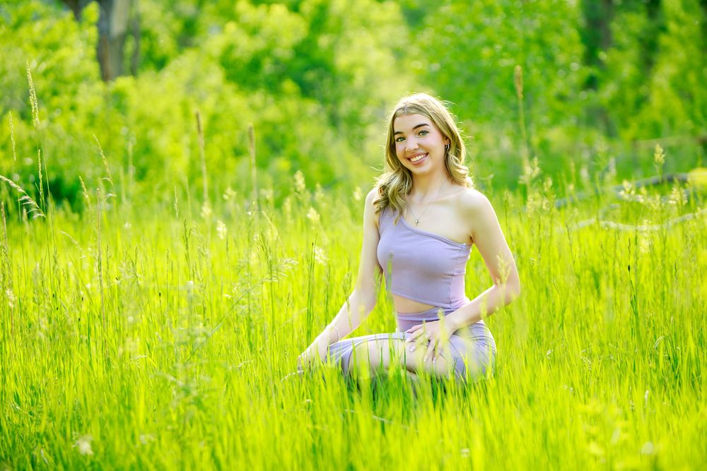 A person in a lavender top sits peacefully in a sunny meadow filled with bright yellow wildflowers.