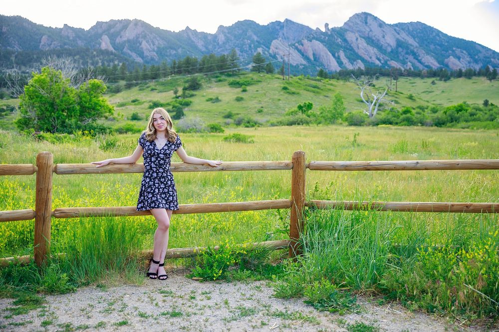 Person in a polka dot dress stands at a wooden fence with the Flatirons mountains of Boulder, Colorado in the background.