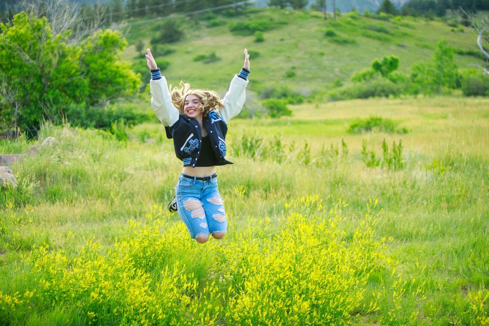 Someone jumps for joy in a vibrant meadow filled with yellow spring wildflowers on a bright sunny day.