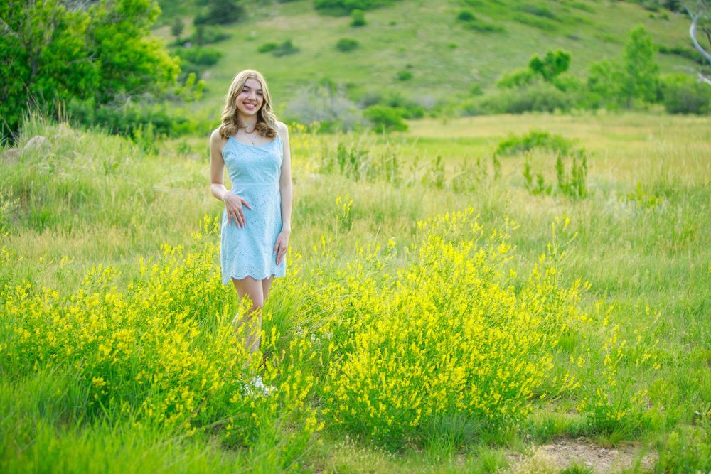 Someone in a light blue dress walks through a vibrant meadow filled with yellow wildflowers and green grass.