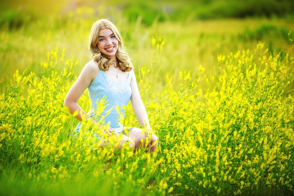 Someone wearing a light blue dress poses in a vibrant field of blooming yellow wildflowers on a sunny spring day.