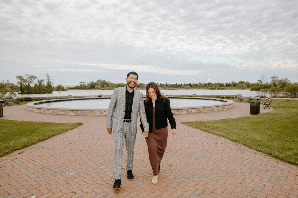 A couple strolling hand in hand along a curved brick pathway with a water feature in the background.