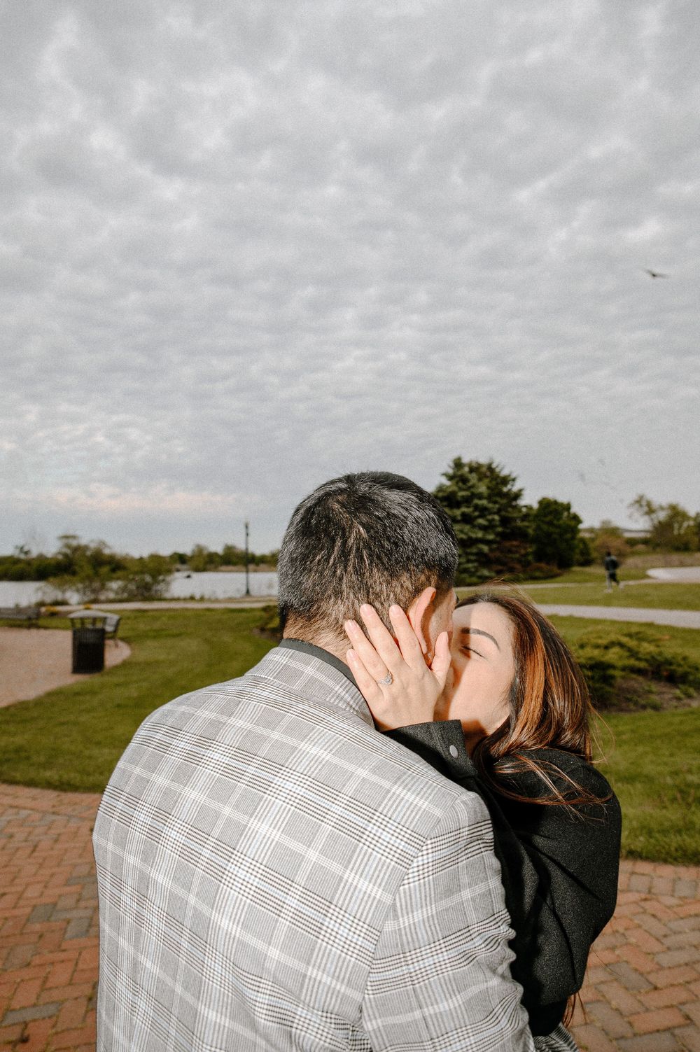 A tender embrace between a couple on a brick path near the water.