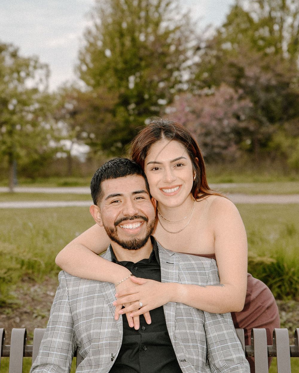 A joyful couple embraces while sitting on a wooden bench in a spring park setting.