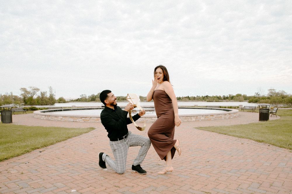 A proposal moment captured on a brick patio with a scenic waterfront backdrop under overcast skies.
