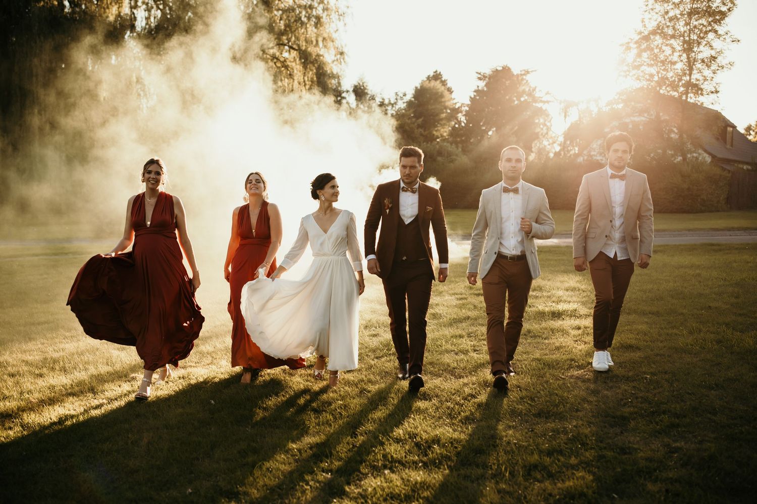 Wedding party walks together through golden sunlit field casting long shadows at sunset.