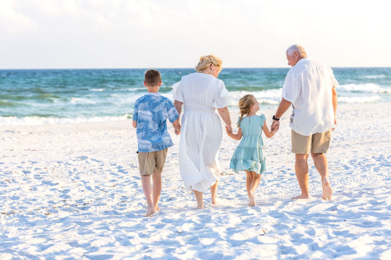 Group in casual summer attire sitting together on a sandy beach with seagrass in the background during golden hour.