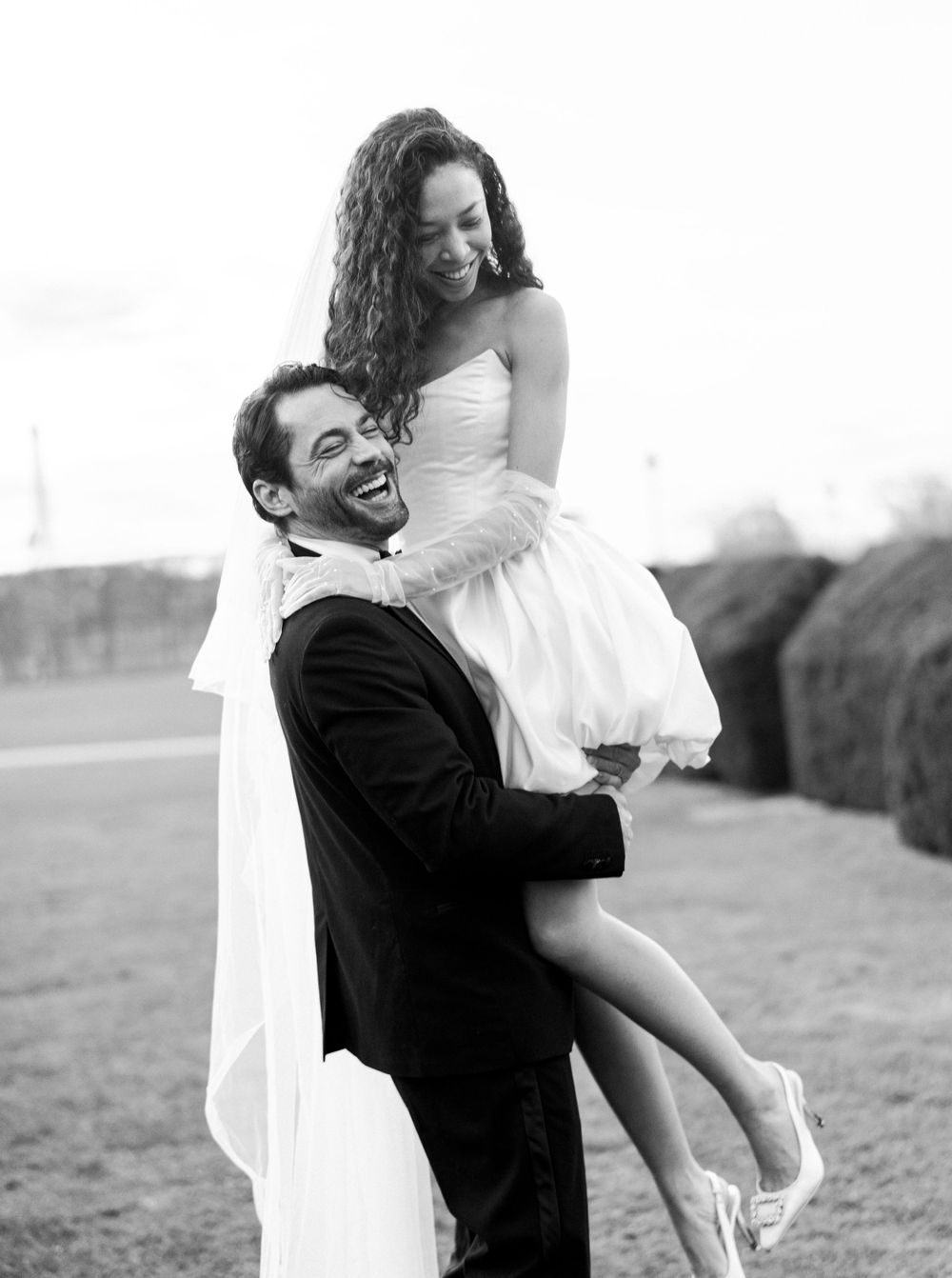 A joyful black and white wedding photo showing a couple embracing outdoors, with the groom lifting the bride. Paris elopement ideas.