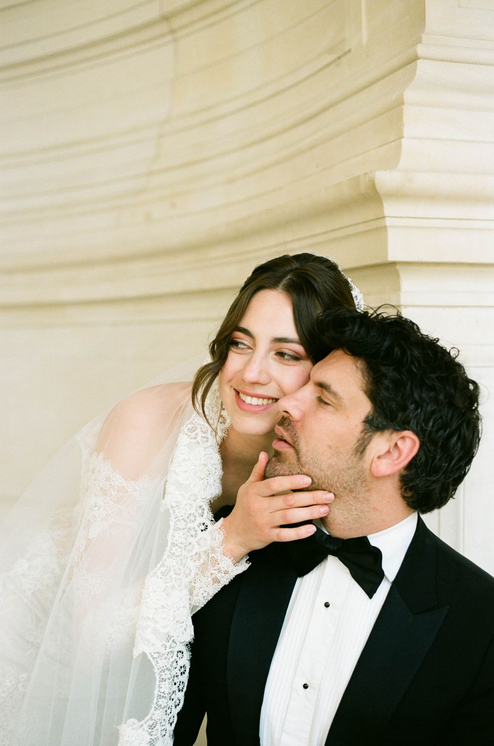A tender moment between newlyweds embracing, with the bride in white lace and the groom in a classic black tuxedo.