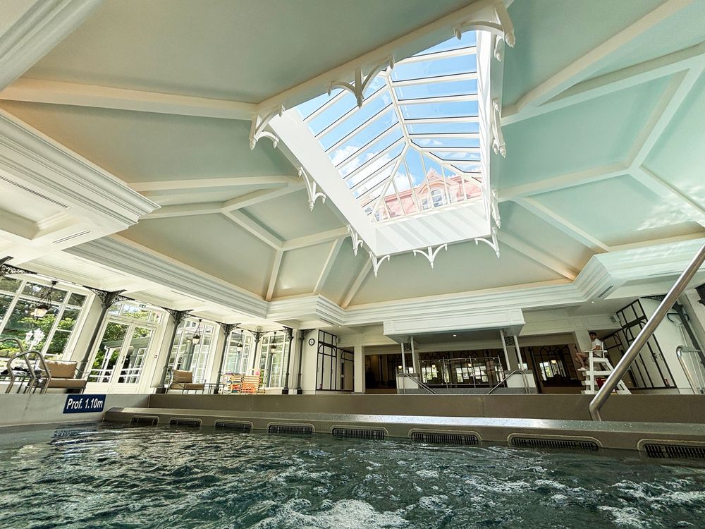 Indoor swimming pool with ornate ceiling, large glass skylight, and architectural details in a luxury spa setting. Disneyland Paris Hotel.