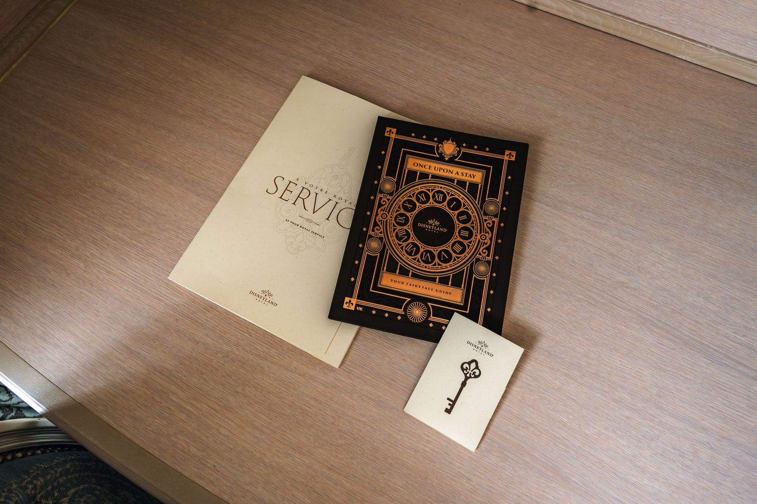 Three items laid out on a wooden desk surface: two books with ornate covers and a small card with a key design. Disneyland Paris Hotel