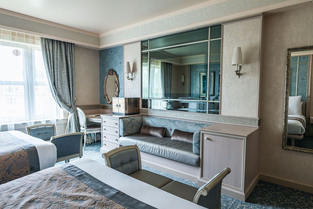 Elegant hotel room interior with mirrored wall, gray sofa, and blue curtains in a contemporary luxurious style.