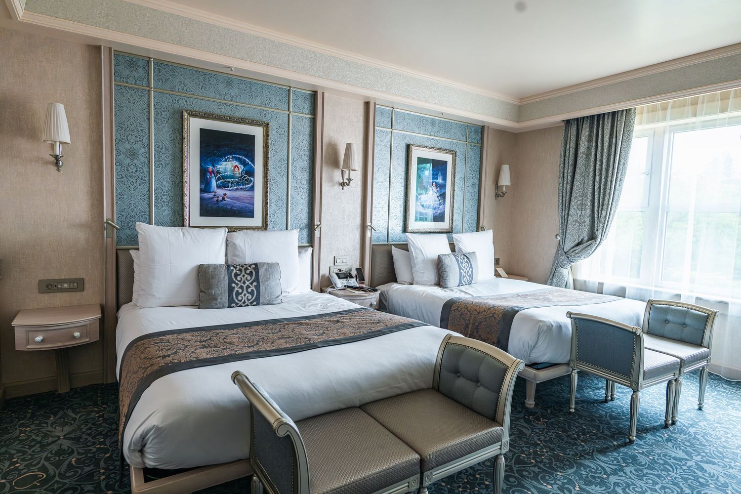Luxurious hotel room with two queen beds, blue artwork, elegant decor and seating area near large window.
