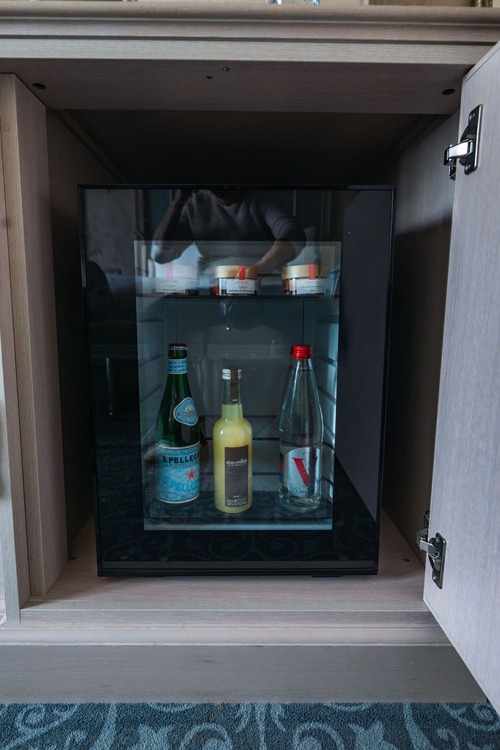 A small mini fridge with glass door displaying various bottled beverages and drinks inside a cabinet compartment.