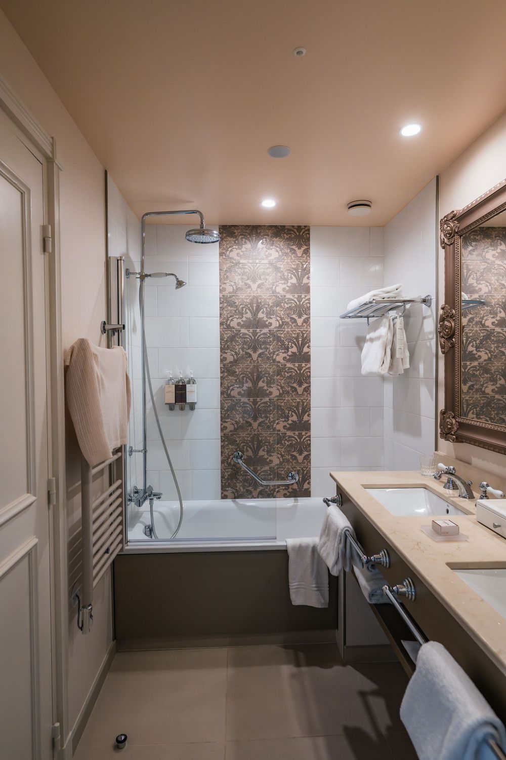 Luxurious hotel bathroom with marble accents featuring a bathtub-shower combo, white tiles, and elegant bronze fixtures.