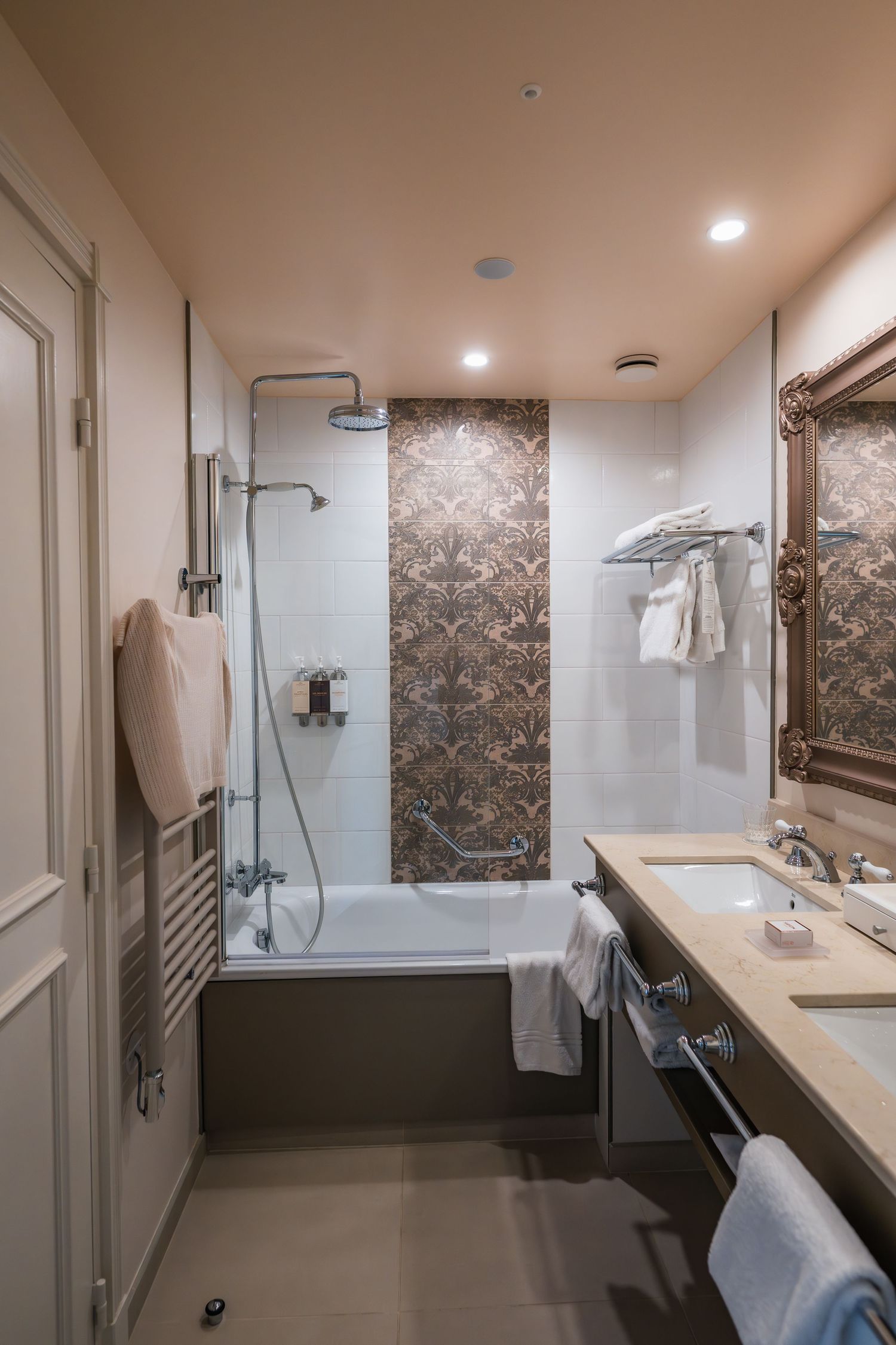 Luxurious hotel bathroom with marble accents featuring a bathtub-shower combo, white tiles, and elegant bronze fixtures.