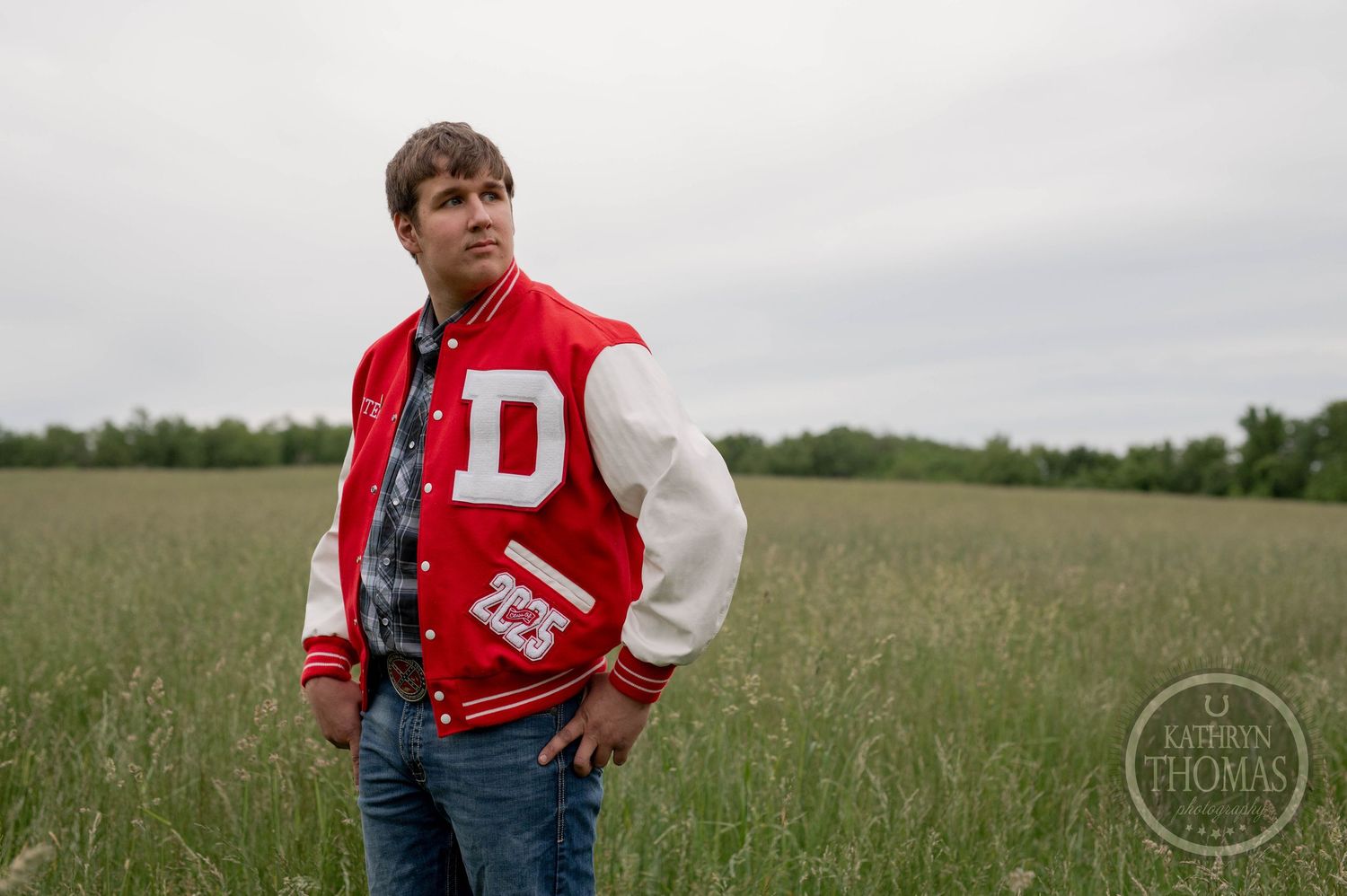 Someone wearing a red and white varsity letterman jacket stands in a grassy meadow field on an overcast day.