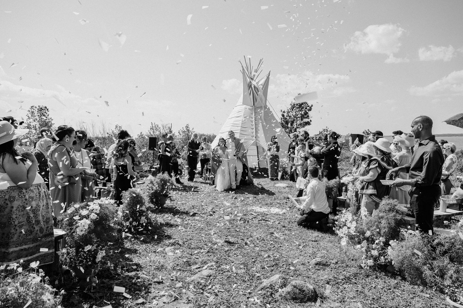 Large crowd of pioneers and settlers gathered in a remote wilderness area amid scattered supplies in black and white.