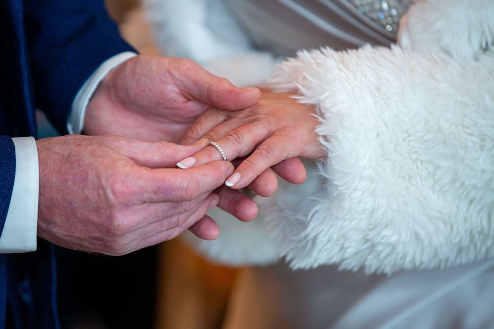 Groom places wedding ring on brides finger during intimate ring exchange ceremony.