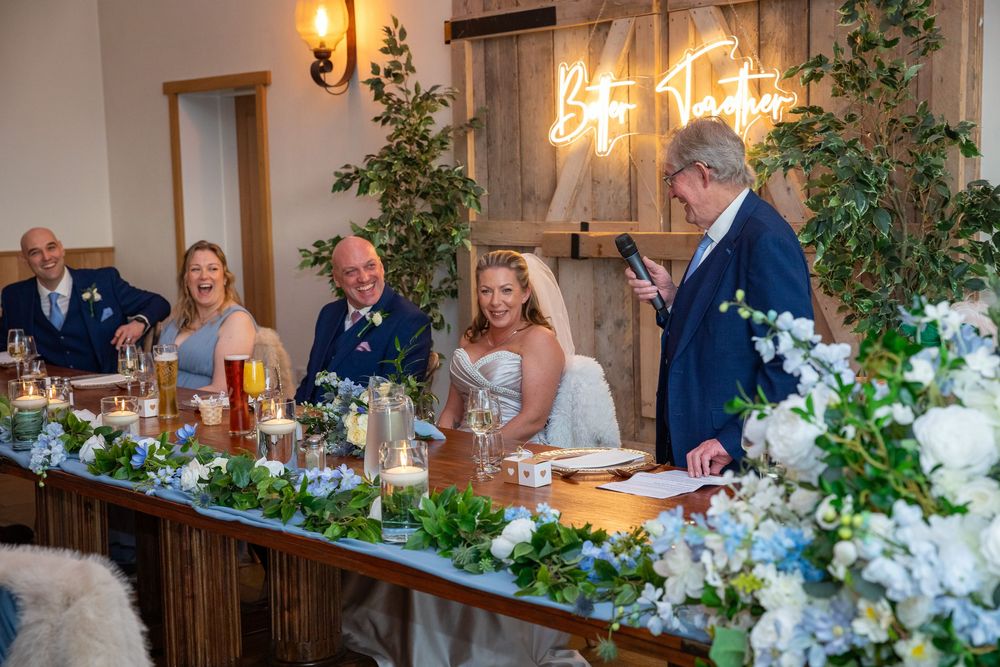 Wedding party laughs during entertaining speech at elegantly decorated floral wedding reception table.