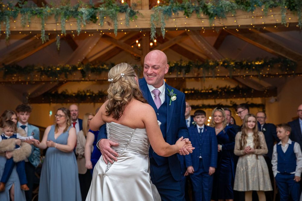 Newlyweds share their first dance together as wedding guests applaud in decorated barn venue.