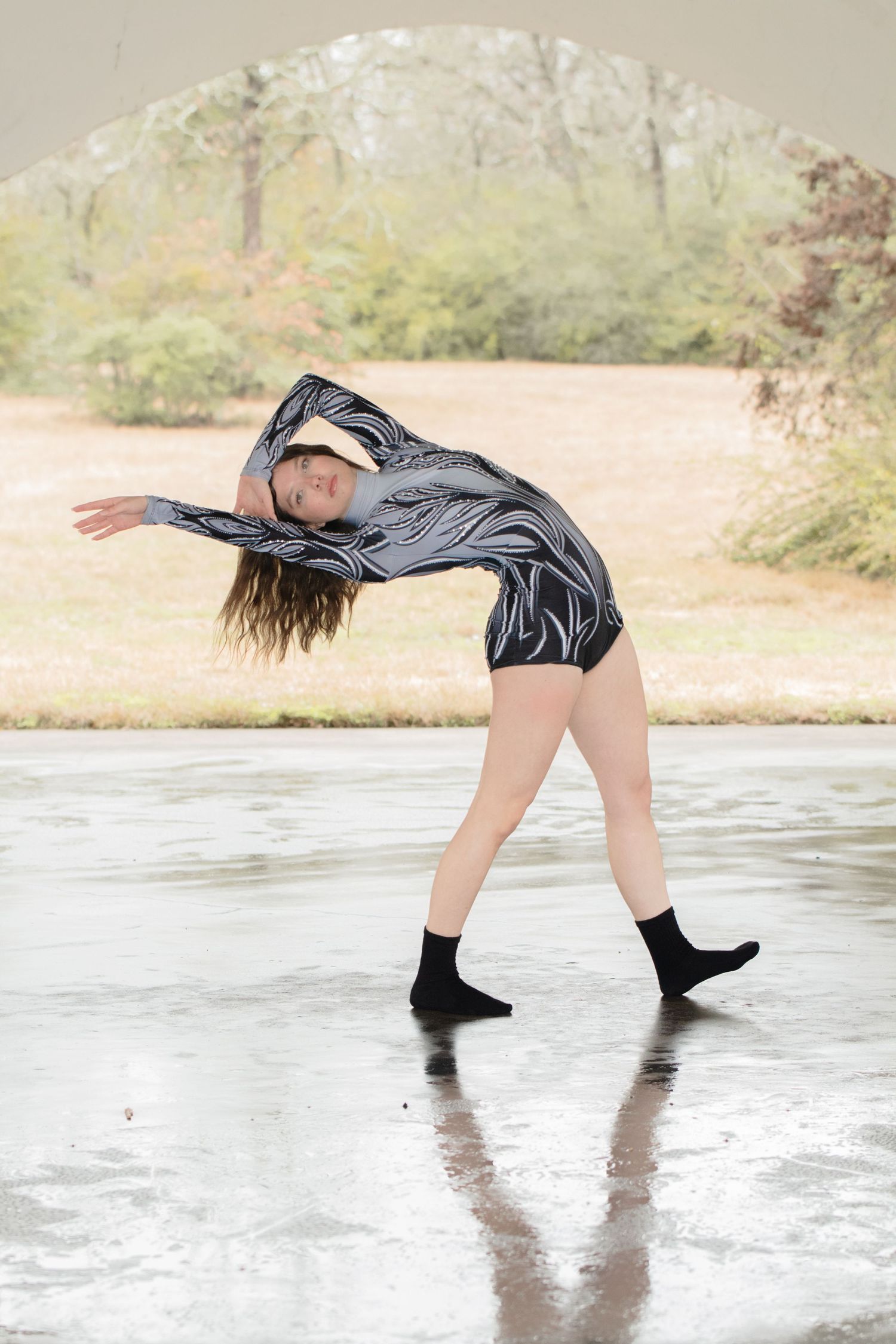 A dancer in black attire performs a series of graceful movements on a reflective surface near water.