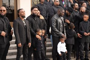 A group of people in dark clothing standing together on steps, including both adults and children.