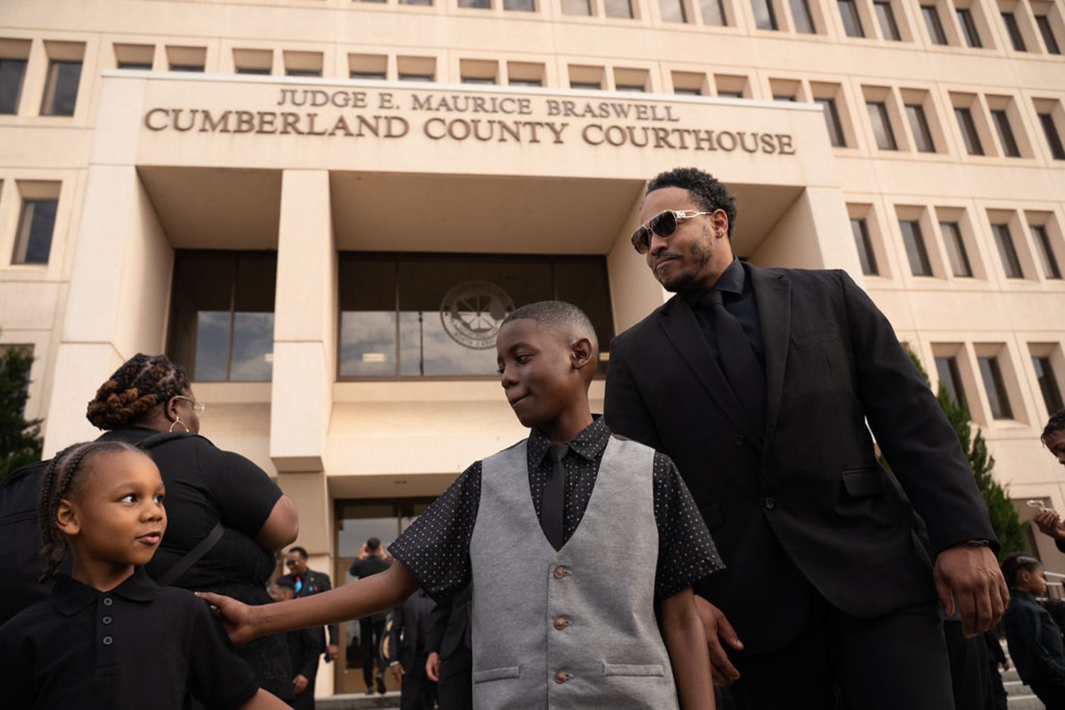 A group of black men stands in warm sunlight outside the front entrance of Cumberland County Courthouse.