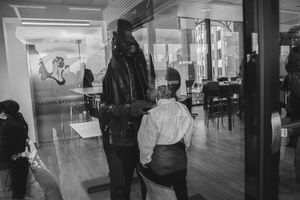 Black and white photo of people in a spacious salon interior with wooden floors and large windows.