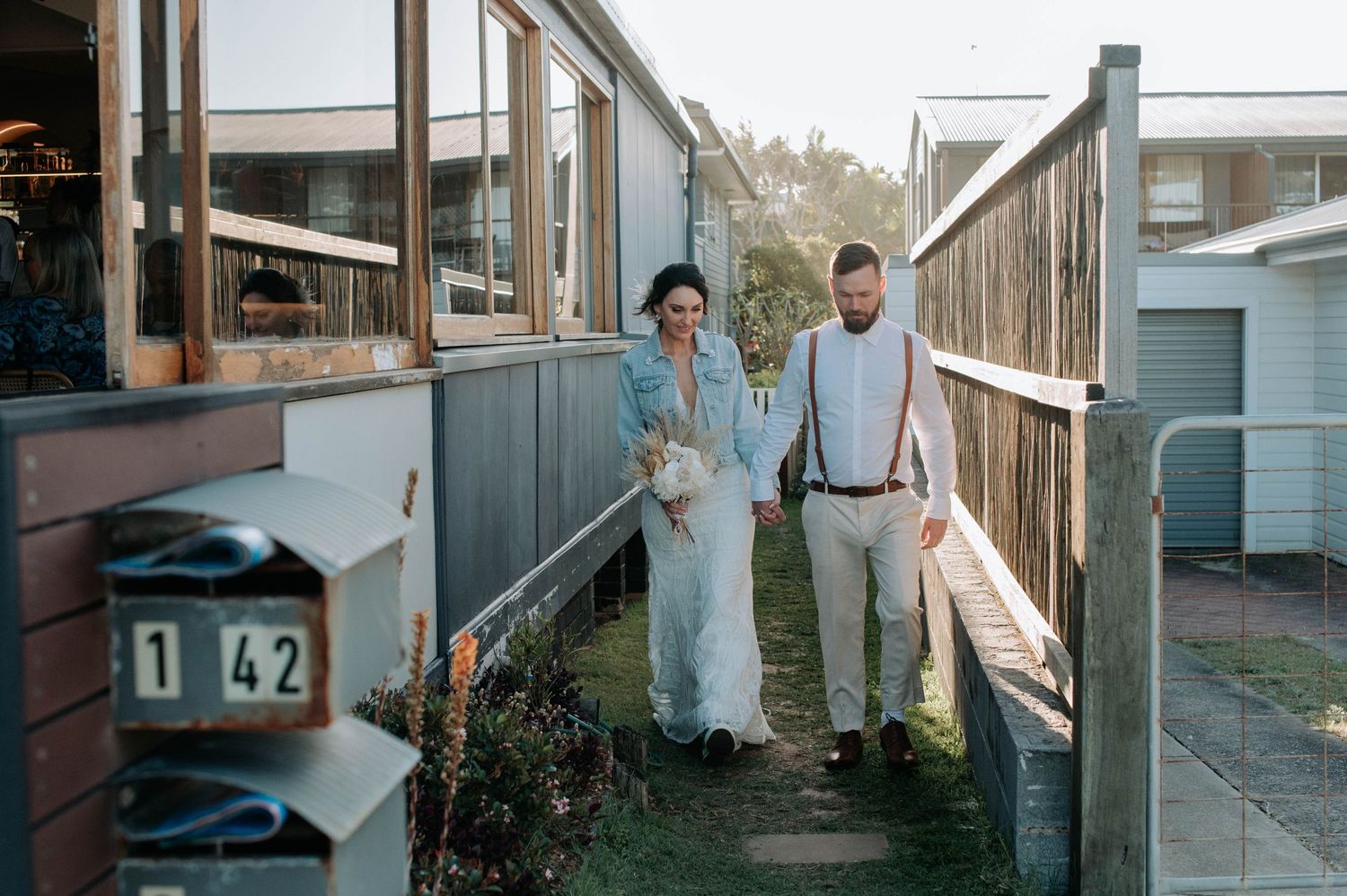 A couple stands together in a vintage-style outdoor hallway wearing casual wedding attire.