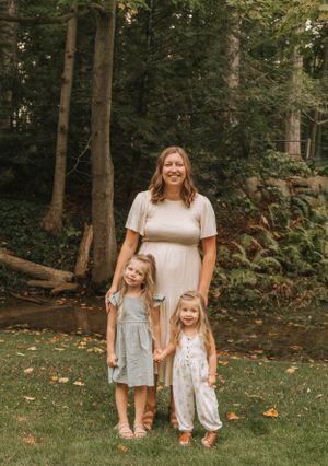 A family poses together in a wooded outdoor setting wearing coordinated neutral-toned outfits.