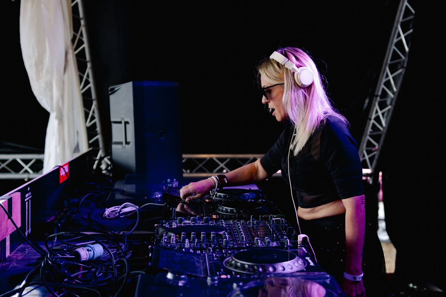 DJ performing behind professional mixing equipment with dramatic purple stage lighting.